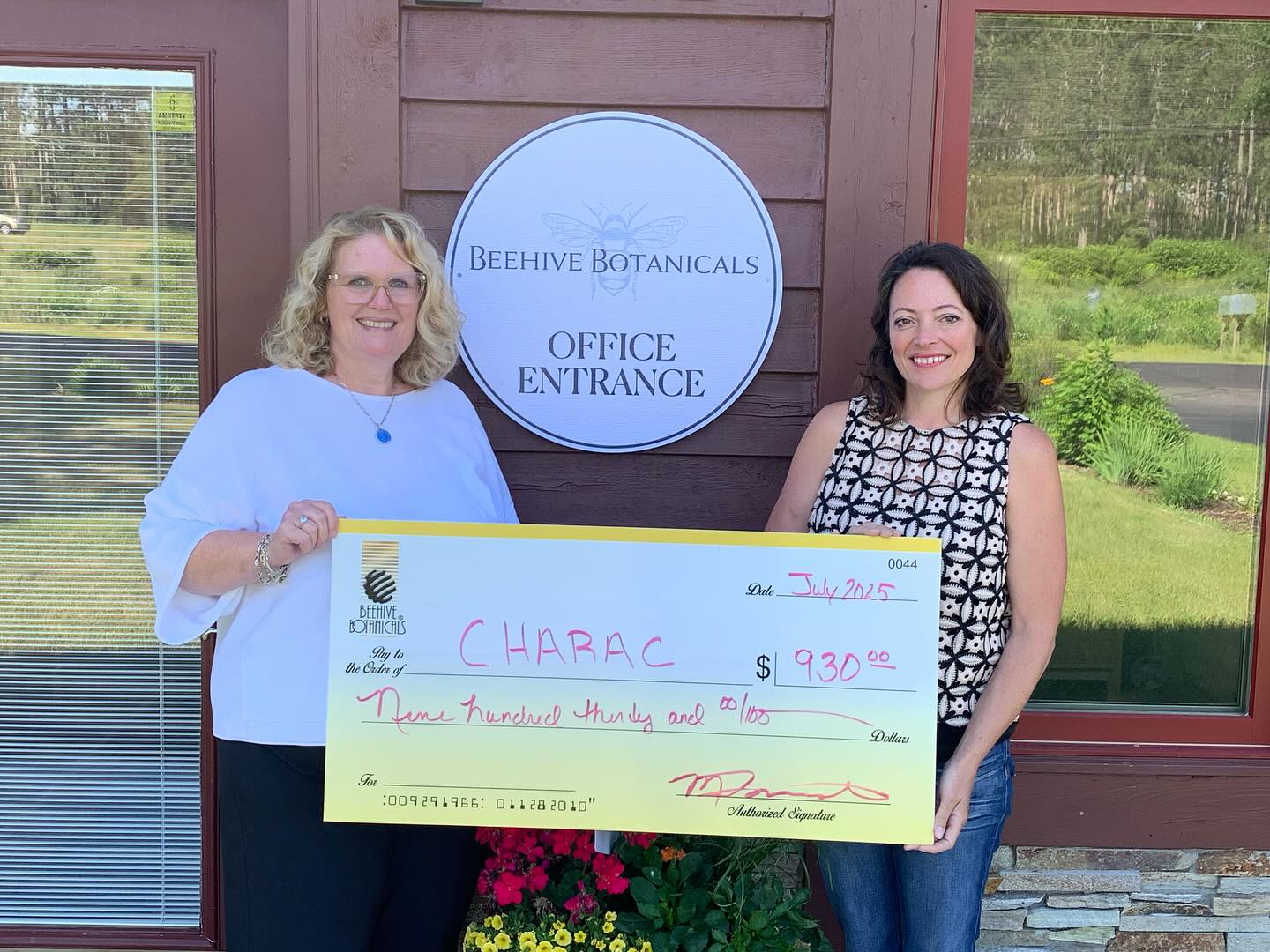 Two women holding a large check in front of a building with 'Beehive Botanicals' signage.