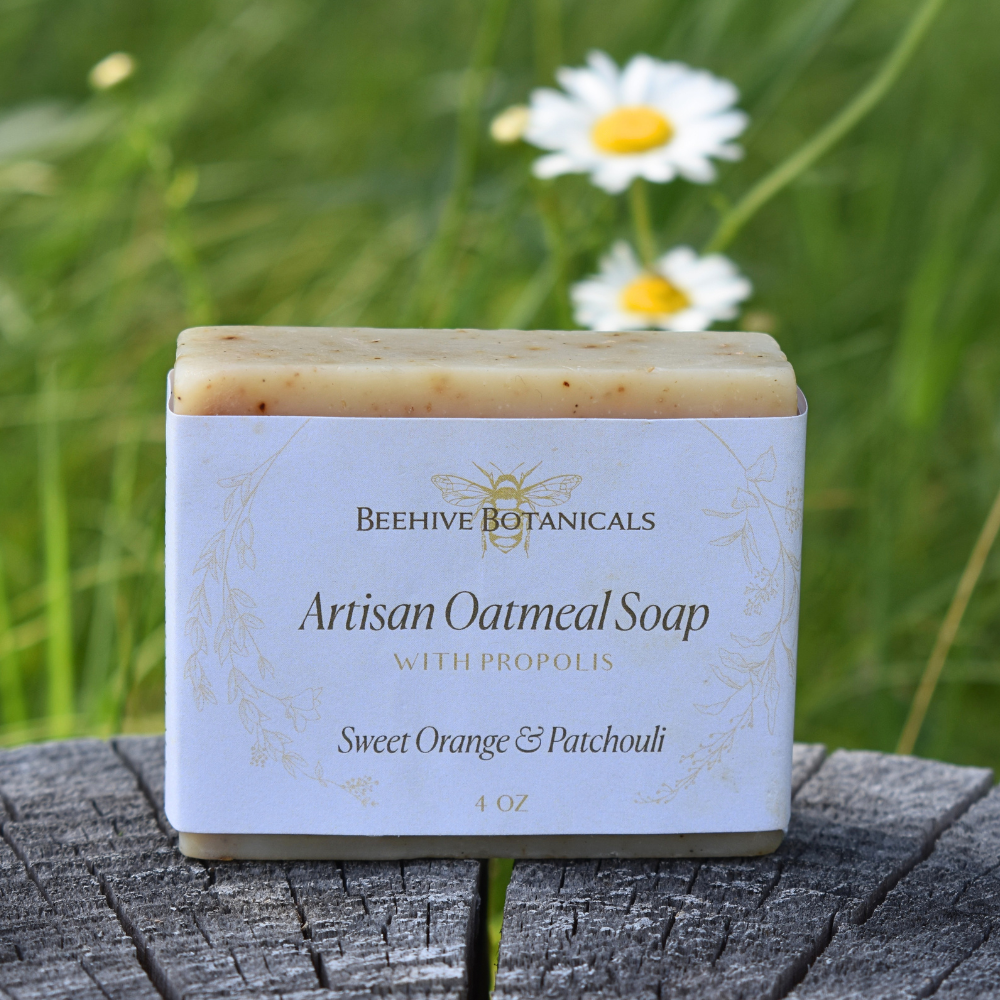 Artisan oatmeal soap with propolis from Beehive Botanicals on a wooden surface with grass and daisies in the background.