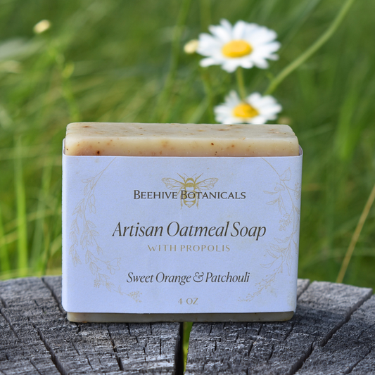 Artisan oatmeal soap with propolis from Beehive Botanicals on a wooden surface with grass and daisies in the background.