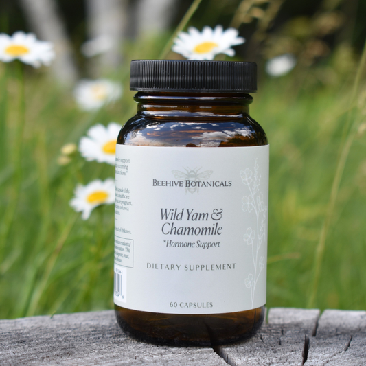 Bottle of Beehive Botanicals Wild Yam & Chamomile supplement on a wooden surface with flowers in the background